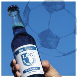 Eine Hand hält "Die Blaue" FCM Fassbrause Hopfen-Holunder mit einer Fußball-Silhouette im Hintergrund